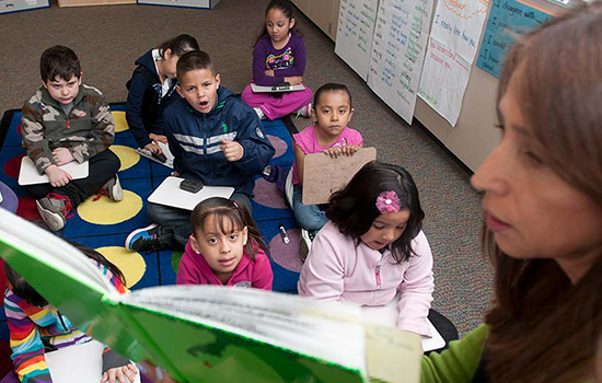 Teacher in foreground reads to elementary school students