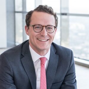 smiling man in a dark suit, wearing glasses