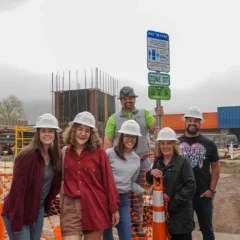 Six individuals wearing hard hats stand in front of a house construction zone.